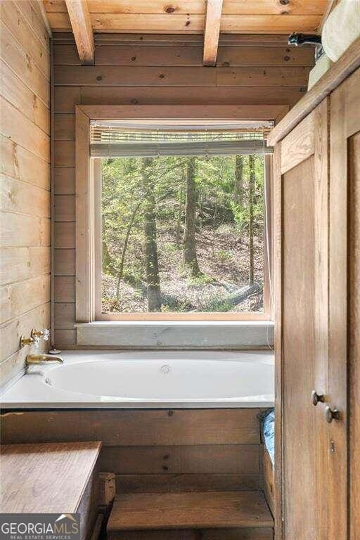 bathroom featuring wooden walls, beamed ceiling, and a healthy amount of sunlight