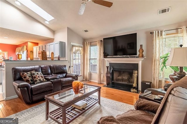 living room featuring a healthy amount of sunlight, light hardwood / wood-style floors, ceiling fan, and a skylight