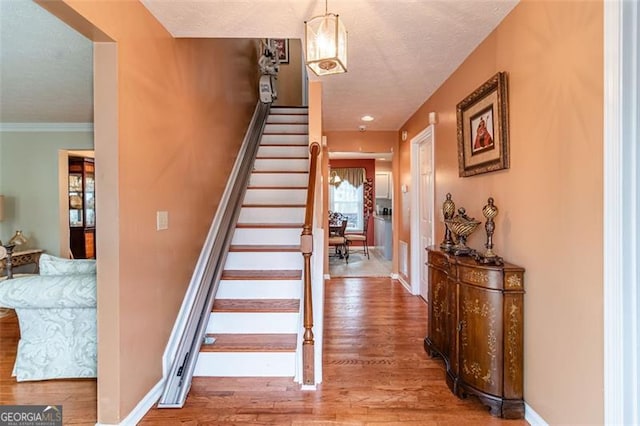 stairway with a textured ceiling, ornamental molding, and hardwood / wood-style floors