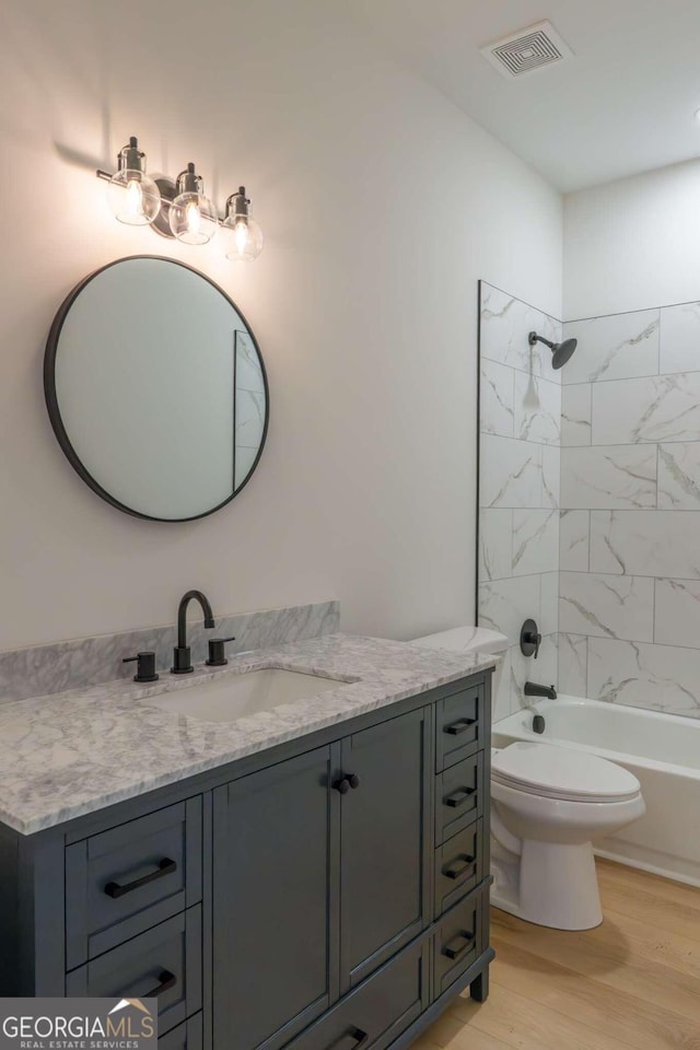 full bathroom featuring wood-type flooring, tiled shower / bath, vanity, and toilet