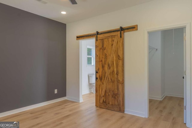 unfurnished bedroom with ceiling fan, light hardwood / wood-style floors, a closet, a spacious closet, and a barn door