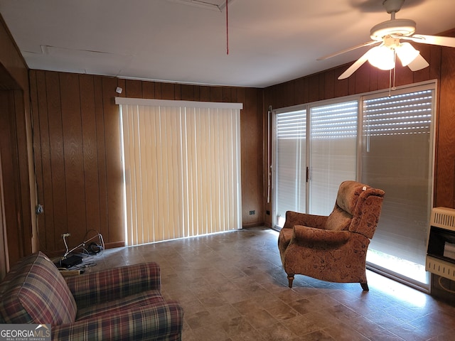 living area featuring wooden walls, ceiling fan, a healthy amount of sunlight, and heating unit