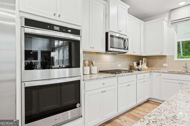 kitchen featuring decorative backsplash, light wood-type flooring, sink, stainless steel appliances, and white cabinetry