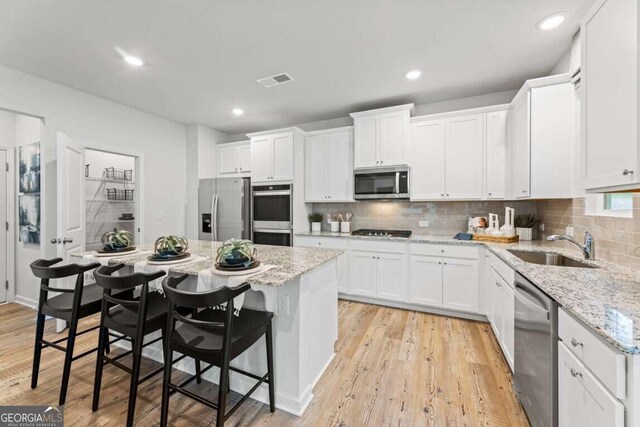 kitchen with light stone countertops, stainless steel appliances, white cabinets, light hardwood / wood-style floors, and a kitchen breakfast bar