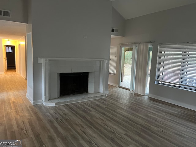 unfurnished living room featuring high vaulted ceiling, a tiled fireplace, and hardwood / wood-style flooring