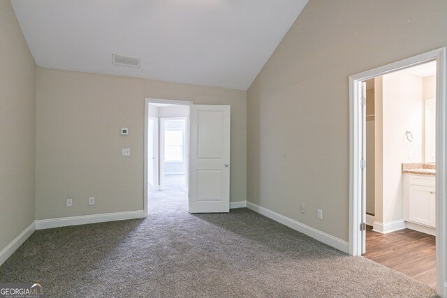 unfurnished bedroom featuring dark carpet, lofted ceiling, and ensuite bathroom