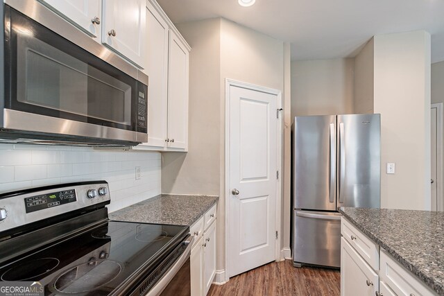 kitchen featuring appliances with stainless steel finishes, dark stone countertops, white cabinetry, and dark hardwood / wood-style flooring