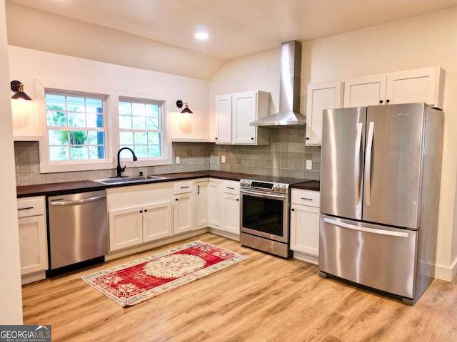 kitchen featuring white cabinets, stainless steel appliances, lofted ceiling, sink, and wall chimney range hood