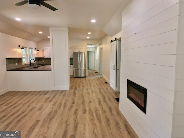 unfurnished living room featuring ceiling fan, lofted ceiling, sink, light hardwood / wood-style flooring, and a barn door