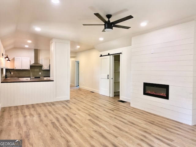 unfurnished living room featuring ceiling fan, sink, a barn door, a large fireplace, and light hardwood / wood-style floors