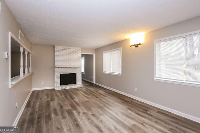 unfurnished living room featuring a brick fireplace, a wealth of natural light, and dark wood-type flooring