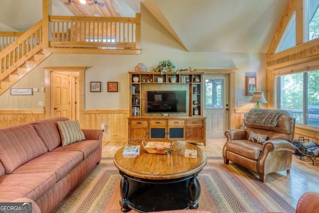 living room with hardwood / wood-style flooring, wood walls, and high vaulted ceiling