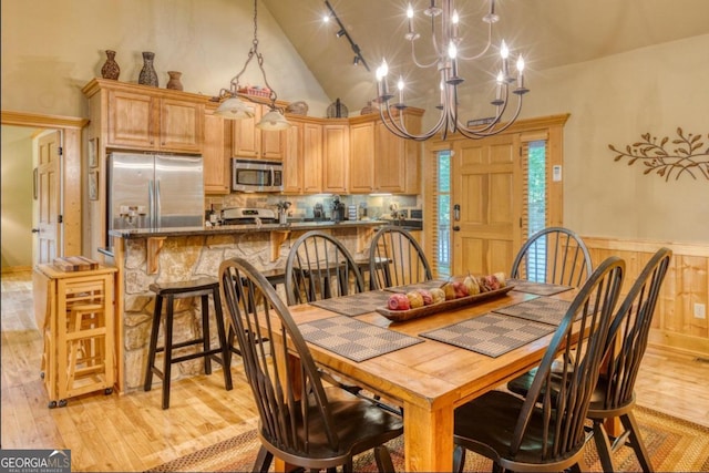 dining space with an inviting chandelier, light hardwood / wood-style flooring, high vaulted ceiling, and rail lighting