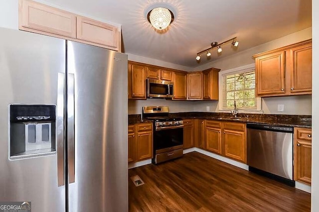 kitchen featuring dark stone counters, appliances with stainless steel finishes, dark wood-type flooring, and sink