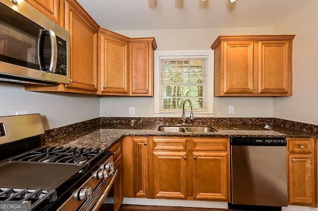 kitchen with appliances with stainless steel finishes, dark stone countertops, and sink