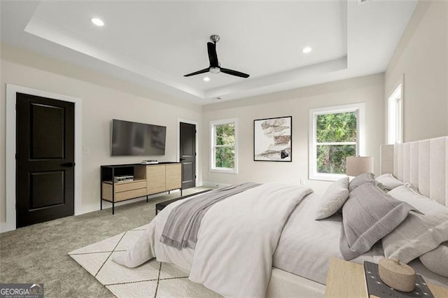 bedroom with light colored carpet, ceiling fan, and a raised ceiling