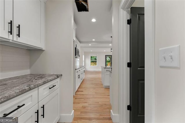 interior space featuring decorative backsplash, light hardwood / wood-style floors, light stone counters, and white cabinets