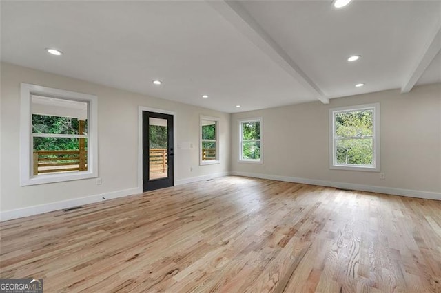 unfurnished living room featuring beamed ceiling, light hardwood / wood-style floors, and a wealth of natural light