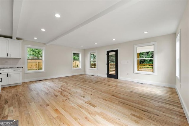 unfurnished living room featuring beam ceiling and light hardwood / wood-style floors