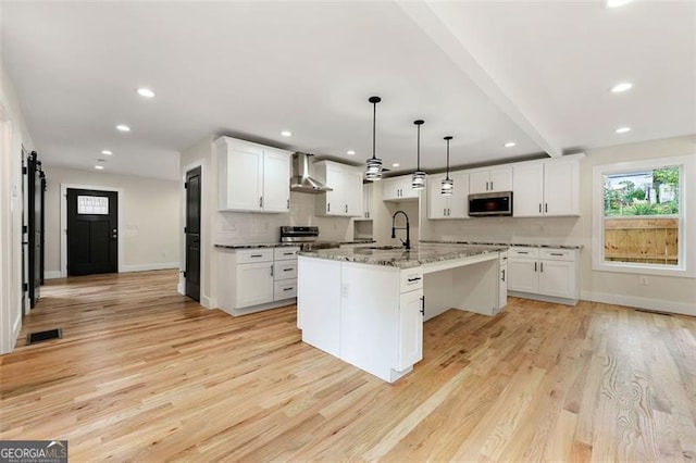 kitchen featuring hanging light fixtures, light hardwood / wood-style floors, white cabinetry, stainless steel appliances, and a center island with sink