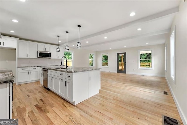 kitchen featuring an island with sink, sink, decorative light fixtures, stainless steel appliances, and dark stone counters