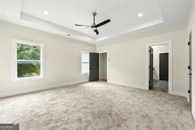 unfurnished bedroom with a raised ceiling, ensuite bath, ceiling fan, and light colored carpet