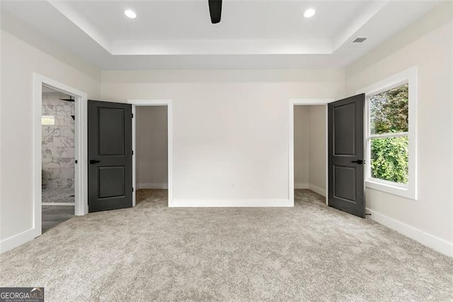 unfurnished bedroom with light carpet, connected bathroom, a tray ceiling, and ceiling fan