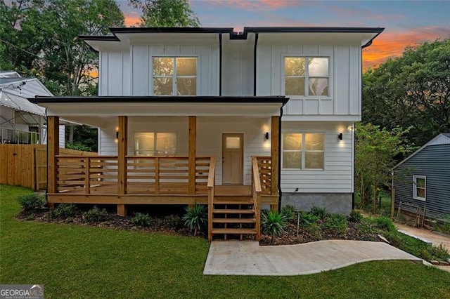 back house at dusk featuring a lawn and a porch