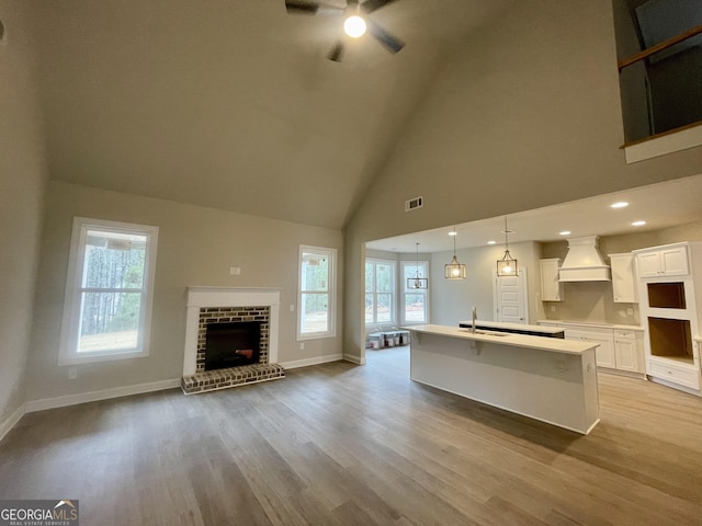 kitchen featuring white cabinetry, an island with sink, custom range hood, decorative light fixtures, and high vaulted ceiling