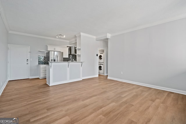 unfurnished living room featuring ornamental molding, stacked washer and dryer, and light hardwood / wood-style flooring