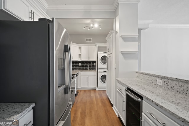 kitchen with stacked washing maching and dryer, white cabinetry, light stone counters, hardwood / wood-style flooring, and stainless steel refrigerator with ice dispenser