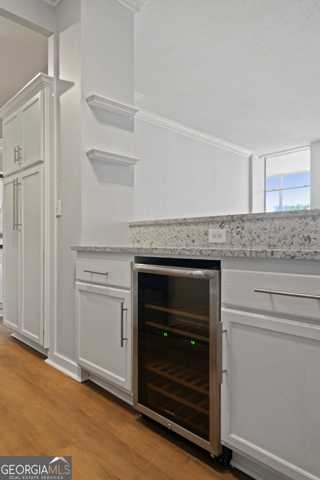 kitchen with light wood-type flooring, wine cooler, light stone counters, white cabinetry, and crown molding