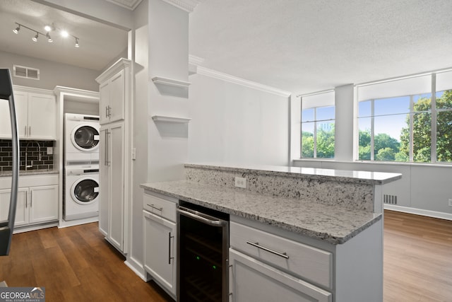 kitchen with white cabinetry, light stone counters, stacked washer and dryer, beverage cooler, and dark hardwood / wood-style floors