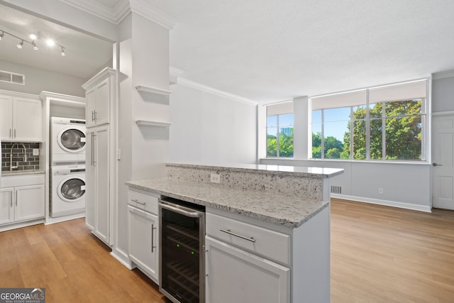 kitchen with light stone counters, white cabinets, beverage cooler, light hardwood / wood-style flooring, and stacked washer and dryer