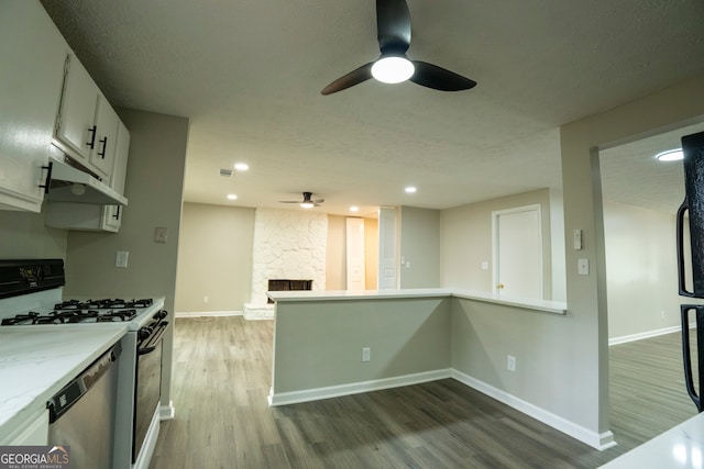 kitchen featuring a stone fireplace, hardwood / wood-style flooring, white gas range oven, stainless steel dishwasher, and white cabinetry