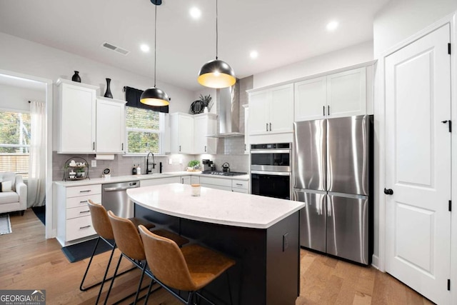 kitchen with pendant lighting, wall chimney range hood, white cabinetry, appliances with stainless steel finishes, and a center island