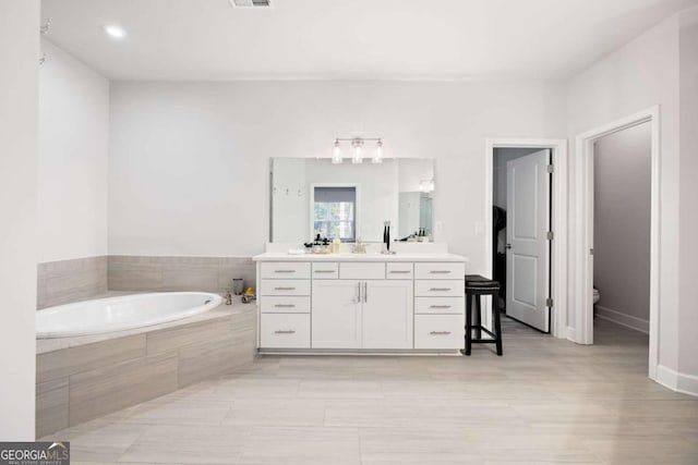 bathroom with vanity, tiled bath, and toilet