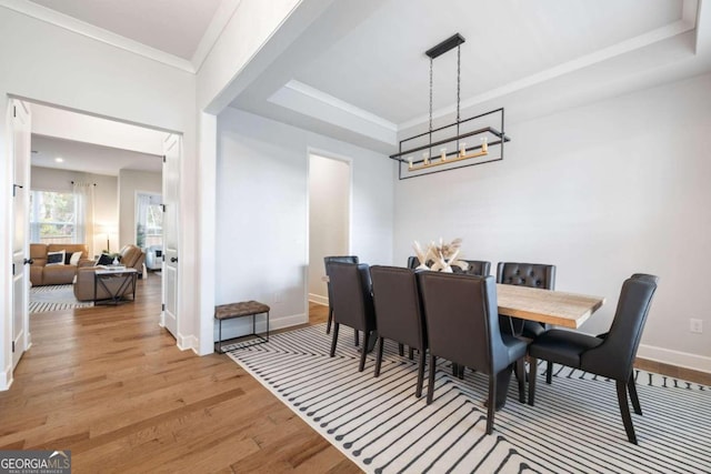 dining area featuring light hardwood / wood-style flooring, crown molding, and a raised ceiling