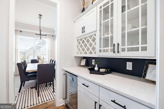 interior space with pendant lighting, wine cooler, white cabinets, light stone countertops, and light wood-type flooring