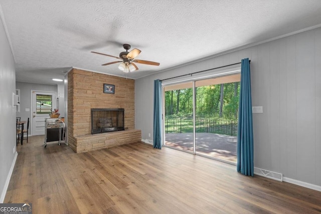 unfurnished living room with wood-type flooring, a stone fireplace, a healthy amount of sunlight, and ceiling fan