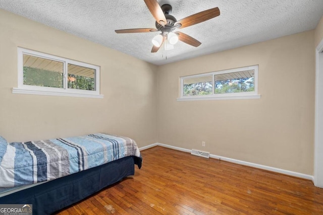 bedroom with ceiling fan, hardwood / wood-style flooring, and a textured ceiling