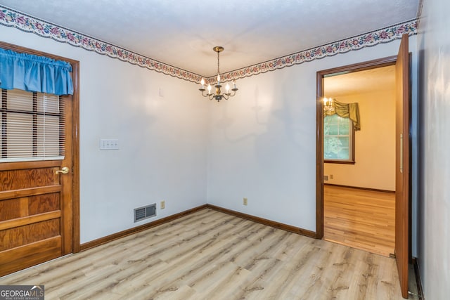 empty room with light hardwood / wood-style flooring and a chandelier