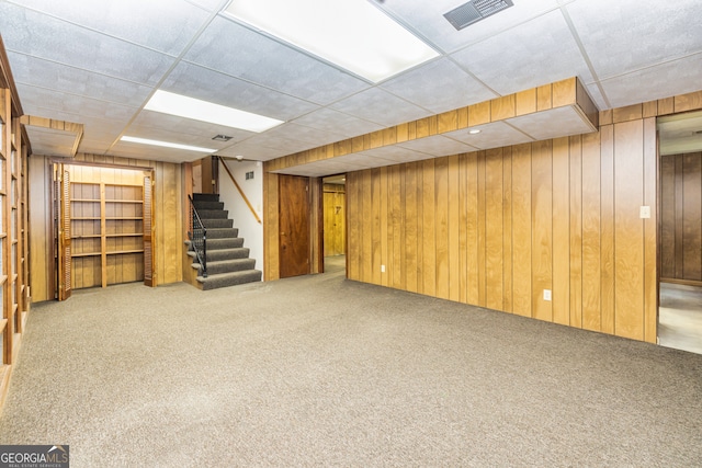 basement with a drop ceiling, wood walls, and carpet flooring