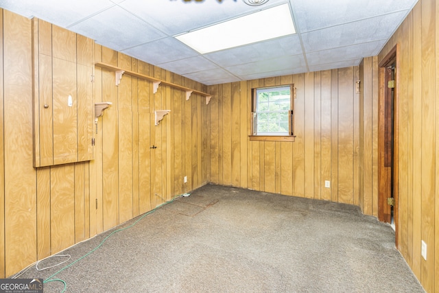 basement with carpet, a drop ceiling, and wood walls