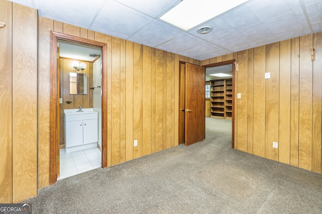 carpeted empty room with wood walls, a paneled ceiling, and sink