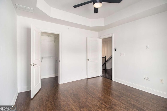 unfurnished bedroom featuring ceiling fan, a closet, dark wood-type flooring, and a tray ceiling