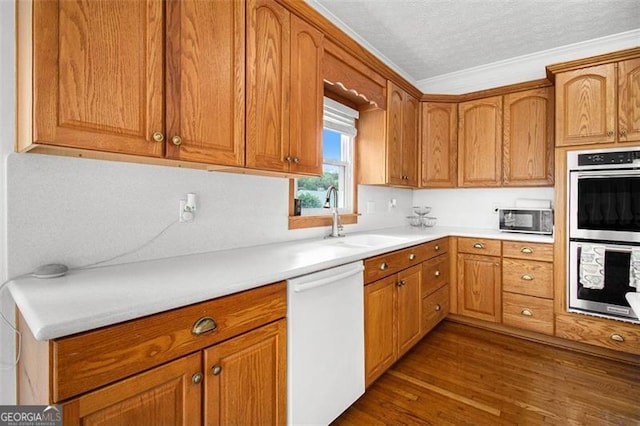 kitchen featuring dark wood finished floors, dishwasher, light countertops, stainless steel double oven, and a sink