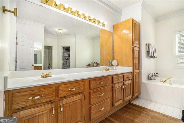 bathroom featuring ornamental molding, tile patterned flooring, tiled tub, and vanity