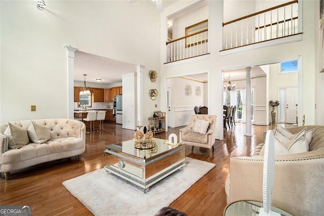 living room with a towering ceiling, ornate columns, dark wood-style floors, and a notable chandelier