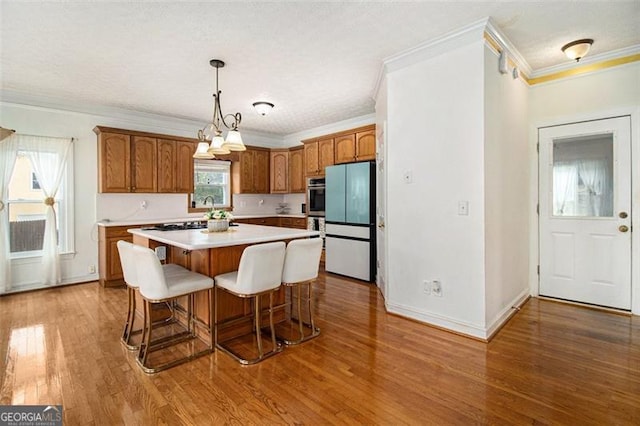 kitchen with wood-type flooring, white refrigerator, hanging light fixtures, a kitchen island, and crown molding